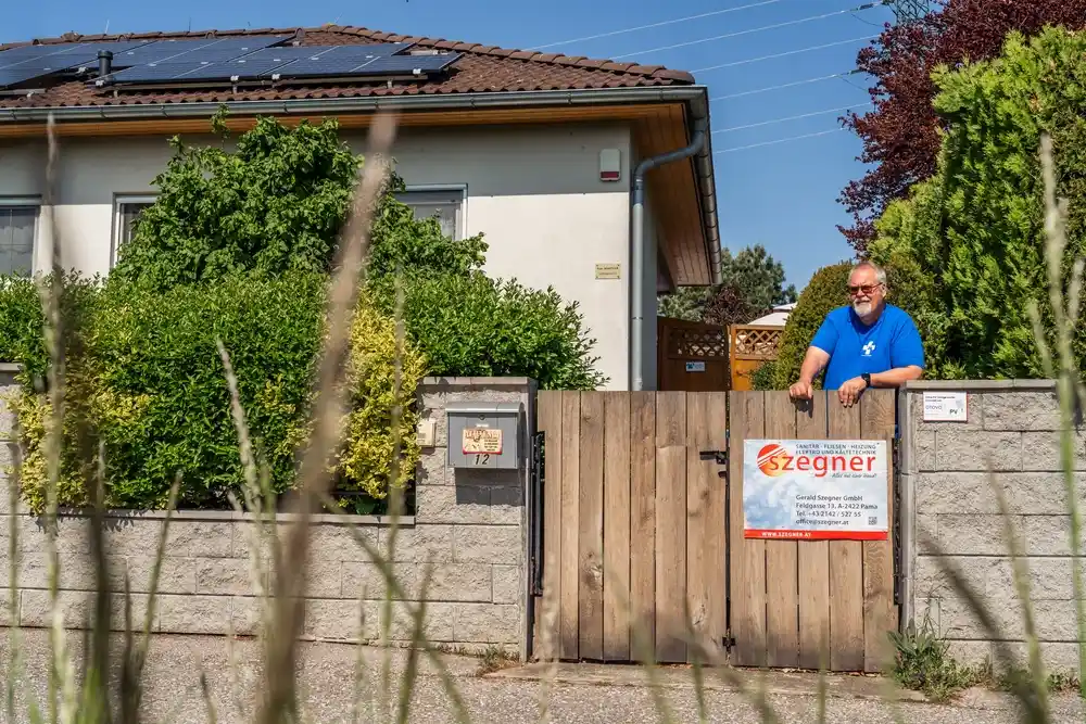 Mann vor seinem Gartentor mit Photovoltaikanlage auf dem Dach des Hauses